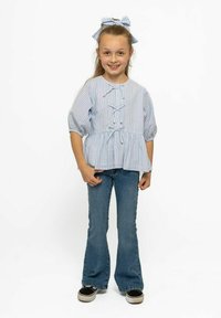Sinine ja valge triibuline Pluus puff-varrukkade ja peplumi vöökoha ning flared denim teksade ja mustade spordijalatsitega. Juuksed on seotud kaunistusse.