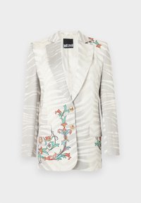 Blazer blanc avec rayures zébrées gris clair, broderie florale colorée sur les poches et l'épaule, deux boutons dorés, étiquette Just Cavalli à l'intérieur.