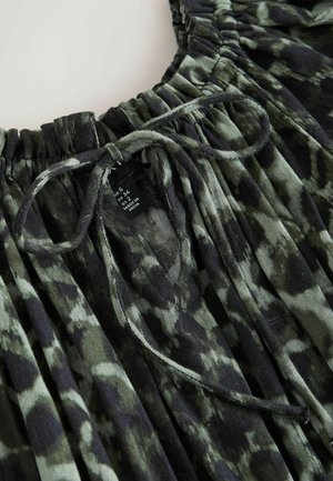 Mørkegrønt og sort tie-dye stof med en elastisk halsåbning med folder og en bundet snor, der viser en tøjstørrelsesmærkat indeni.