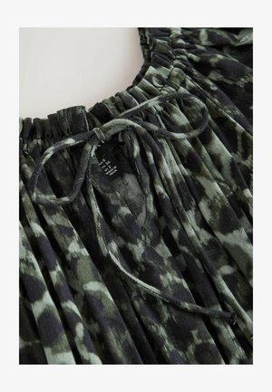 Tissu tie-dye vert foncé et noir avec un col élastique froncé et un nœud de cordon noué, montrant une étiquette de taille de vêtement à l'intérieur.