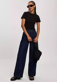 Czarna dopasowana koszulka, wysoko w talii szerokie ciemnoniebieskie dżinsy, czarne wysokie sandały i mała czarna torba. Dodatki to okulary przeciwsłoneczne.