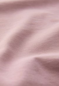 Tissu mauve clair et doux avec une texture côtelée fine et des plis délicats créant des variations d'ombre subtiles sur la surface.
