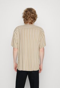 Camicia a maniche corte beige a righe con linee verticali bianche, vestibilità comoda e orlo arrotondato, realizzata in tessuto leggero.