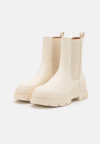 Stivaletti beige alla caviglia realizzati in morbida pelle sintetica, con suole in gomma spesse e robuste e pannelli laterali elastici. Anelli di trazione sul retro.