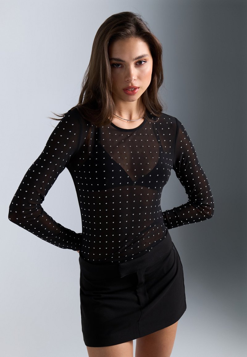 Svart gjennomsiktig langermet topp med små sølvnagler, med en tettsittende design og scoop hals, parret med et svart miniskjørt.