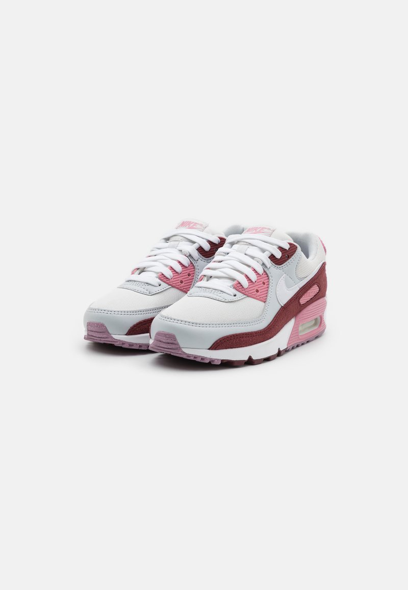Le sneaker Nike Air Max 90 presentano una tomaia in pelle bianca con accenti rosa e bordeaux, patch in suede testurizzato e un'unità di ammortizzazione ad aria visibile.