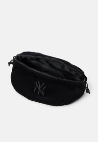 Svart kordfløyelpung med en glatt innside, glidelås og preget New York Yankees-logo foran. Rund form og teksturert overflate.