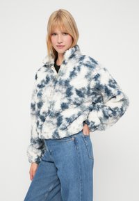 Sudadera de forro polar en un patrón de teñido anudado en blanco y azul, con un alto cuello y detalle de cremallera dorada, y una textura suave y esponjosa.