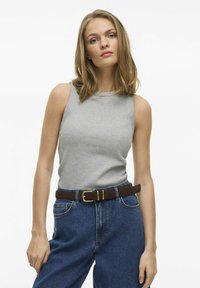 Grå ärmlös topp av ribbad tyg, parat med högmidjade blå denimbyxor och ett brunt bälte med en guldfärgad spänne.