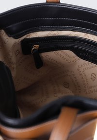 Interieur van een bruine leren handtas met beige stofvoering, een zwarte ritsvak en herhaalde "CAFÉNOIR" logo print.