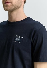 T-shirt in cotone blu navy con scollatura tonda, caratterizzato da una piccola etichetta con il marchio sul petto. Texture liscia e vestibilità standard.