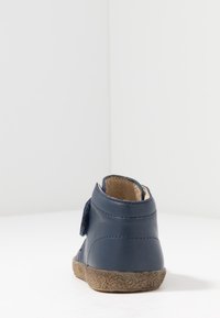 Stivaletto in pelle blu navy con suola beige testurizzata, dotato di cinturino in velcro per la chiusura e dettagli cuciti sui lati.