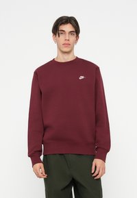 Burgundská mikina Nike s okrúhlym výstrihom, dlhými rukávmi a malým bielym logom na hrudi. Hladká tkanina, voľný strih a rebrované manžety.
