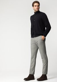 Czarny kardigan z guzikami, w zestawieniu z jasnoszarymi spodniami w kratę i brązowymi botkami za kostkę. Ubranie charakteryzuje się dopasowanym krojem i gładką fakturą.