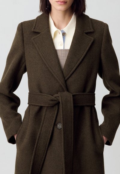 Cappotto verde oliva in misto lana con vita cintata, colletto a rever e due tasche frontali. Presenta una chiusura con un solo bottone e una vestibilità sartoriale.