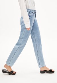 Jeans de tiro alto en azul claro con un corte recto y costuras visibles, combinados con sandalias de plataforma negras con una correa ajustable.