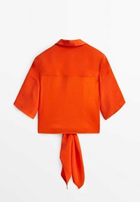 Chemise à manches courtes et courte en satin orange vif, avec un col droit et un détail à nouer au dos. Texture lisse, design minimaliste.