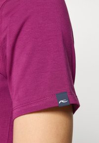 Lila Kurzarm-T-Shirt aus weichem Stoff, mit einem blauen Etikett und einem weißen Logo auf dem Ärmel. Glatte Textur mit minimalen Nähten.