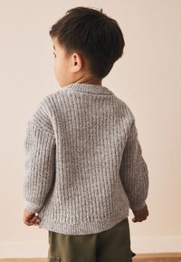 Grå strikket sweater med ribbet struktur, rund halsudskæring og lange ærmer, båret af et barn mod en neutral baggrund.