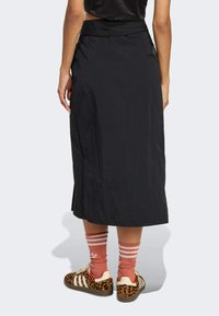 Czarna spódnica o średniej długości, wykonana z lekkiego materiału, z gładką teksturą i bocznym rozcięciem. W połączeniu z trampkami w panterkę i paskowanymi skarpetkami.