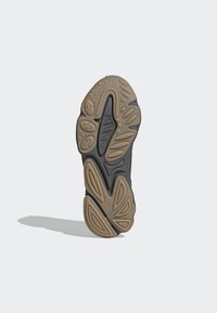 Shoe sole featuring a textured design with dark gray and tan colors. Notable grooves and rounded shapes for grip and support.