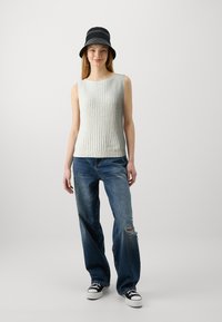 Light gray ribbed sleeveless top paired with distressed blue wide-leg jeans and black bucket hat. White sneakers complete the outfit.