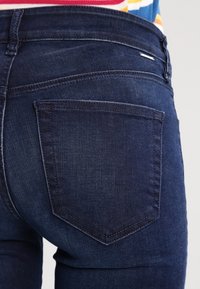 Mörkblå denimjeans har en enkel bakficka med en subtil sydd design, slät textur och klassisk avsmalnande form.