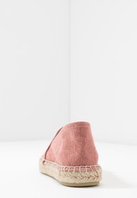 Espadrille rose avec tige en tissu, semelle en jute, talon arrondi et détails cousus le long du bord.