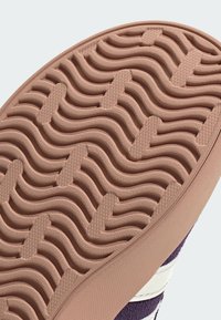 Suola in gomma per sneaker di un rosa chiaro con motivi a onde e a punti. Presenta una superficie testurizzata per garantire aderenza, insieme a una tomaia in suede viola.