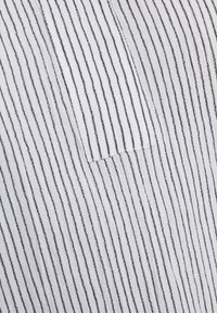 Tissu rayé présentant des lignes alternées noires et blanches, avec une surface texturée et une petite poche sur un côté.