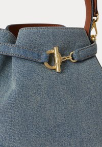 Τσάντα χειρός από τζιν με καφέ δερμάτινο λουρί, με κούμπωμα σε χρυσή απόχρωση χαραγμένο με τα αρχικά "RL", κοντινή λήψη στα υφάσματα και τις μεταλλικές λεπτομέρειες.