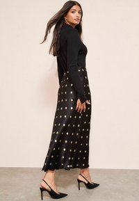 Fekete, hosszú szoknya arany pöttyökkel, selyemfényű és lágy esésű. Fekete, testhezálló pulóverrel és fekete magassarkú cipővel párosítva.