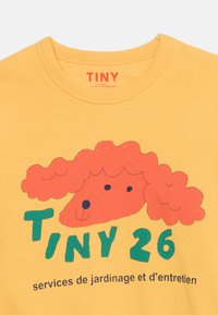 Κίτρινο πουκάμισο με κόκκινη εικονογράφηση σκύλου με σγουρά μαλλιά και πράσινο κείμενο "TINY 26" πάνω από τη γαλλική φράση "services de jardinage et d'entretien."