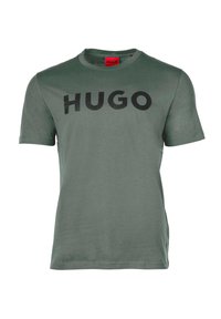 Olíva zöld pamut póló, kerek nyakkal és rövid ujjakkal, melyen a "HUGO" szó fekete színben, hangsúlyosan látható elöl.