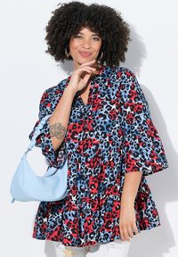Tunica a fantasia rossa, blu e nera con scollo a V, maniche a campana e design arricciato. Abbinata a una borsa a spalla azzurro chiaro.