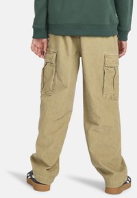 Khaki Cargo-Hosen aus strapazierfähigem Stoff, mit zwei seitlichen Taschen, einer lockeren Passform und einer strukturierten Oberfläche. Die Rückansicht zeigt die Platzierung der Taschen.