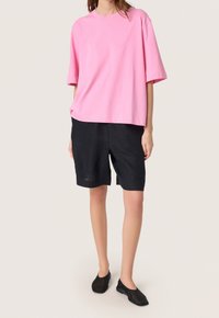 Camiseta de algodón rosa de gran tamaño con mangas cortas, combinada con pantalones cortos de lino negros y zapatos negros tipo slip-on. Diseño sencillo y ajuste relajado.