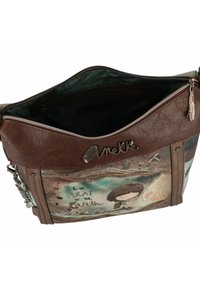 Braune Handtasche aus Kunstleder mit künstlerischem Design. Sie verfügt über einen Reißverschluss, eine grüne Innenauskleidung und dekorative Akzente wie einen Anhänger und gestickte Details.