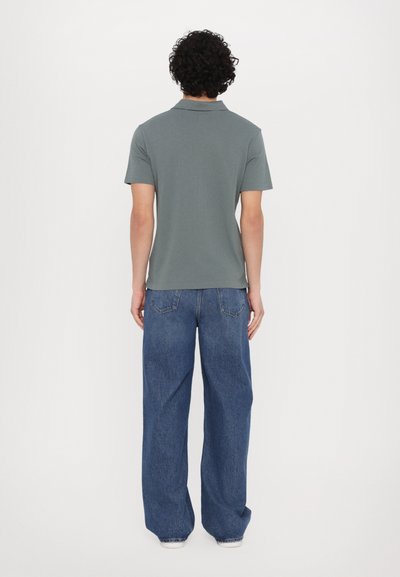 Gray short-sleeve polo shirt with a straight-cut design, paired with loose-fitting blue denim jeans and a subtle back ribbed texture.