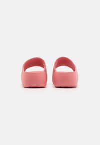Calzado rosa con un diseño de espalda abierta y forma redondeada. Fabricado con un material suave sin patrones o acentos visibles. Suela plana con textura mínima.