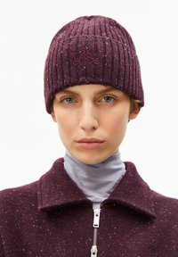 Bordeaux gebreide beanie met geribbelde textuur, met een klein geborduurd logo aan de voorkant. Draag het met een collared kledingstuk eronder.