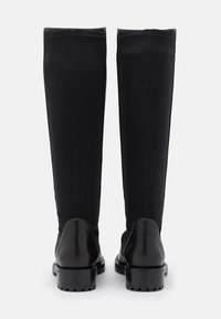 Bottes noires montant jusqu'au genou, avec une partie inférieure en cuir lisse et une partie supérieure en tissu extensible, dotées d'un bout arrondi et d'une semelle épaisse.