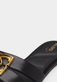 Sandale à glissière en cuir noir avec semelle rembourrée et boucle décorative métallique dorée sur une large bride.