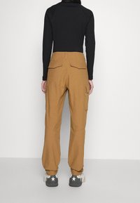 Bruna cargobyxor med en avslappnad passform, utrustade med flera fickor och ett texturerat tyg, kombinerat med grå sneakers med vita detaljer.