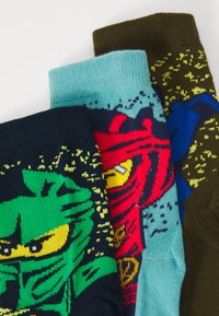 Drei Paar Socken: grün mit katzenmotiv, blau mit einem Muster und dunkelbraun mit gelben Akzenten. Jedes Paar hat farbenfrohe, gewebte Grafiken.