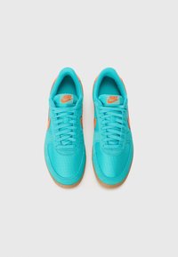 Zapatillas Nike turquesas con acentos en naranja, que cuentan con un upper texturizado, diseño de cordones y suela de goma.