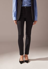 Jeans skinny negros de mezclilla, con una cintura alta y un ajuste slim, combinados con una camisa azul y tacones negros de punta.