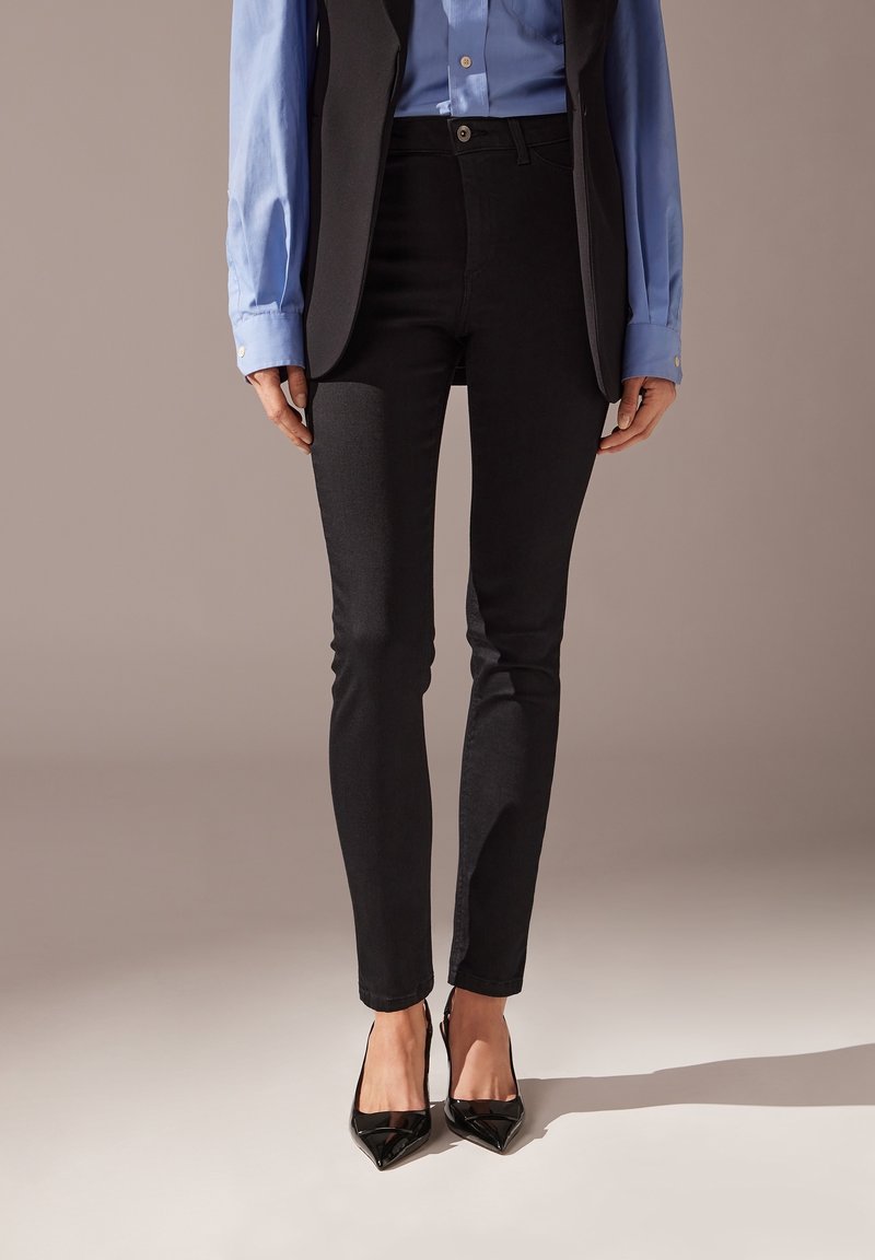 Jeans skinny negros de mezclilla, con una cintura alta y un ajuste slim, combinados con una camisa azul y tacones negros de punta.