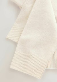 Pulover crem, cu o textură moale, manșete ribbate și un design minimalist. Materialul pare cald și ușor.