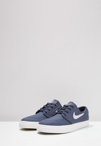 Un paio di sneaker basse Nike blu navy con logo swoosh bianco e suole in gomma bianca su una superficie bianca.